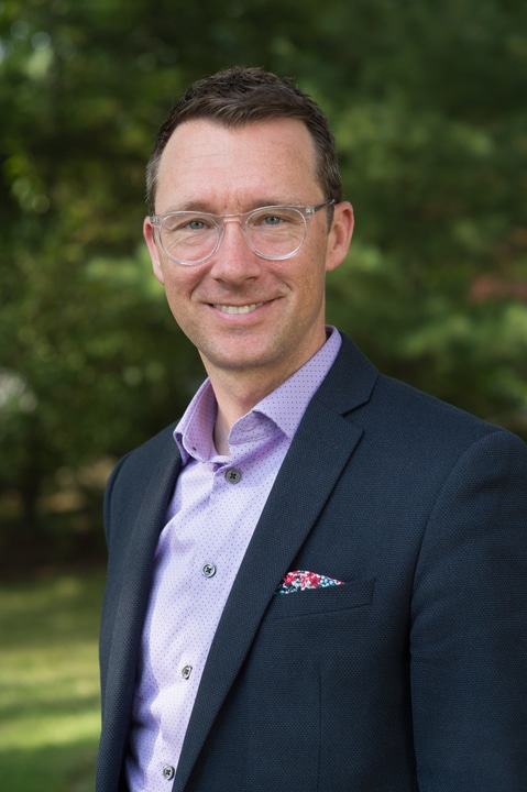 Headshot of man in navy suit and lavender dress shirt